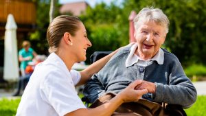 Nurse holding hands with senior woman sitting in wheelchair in garden of retirement home